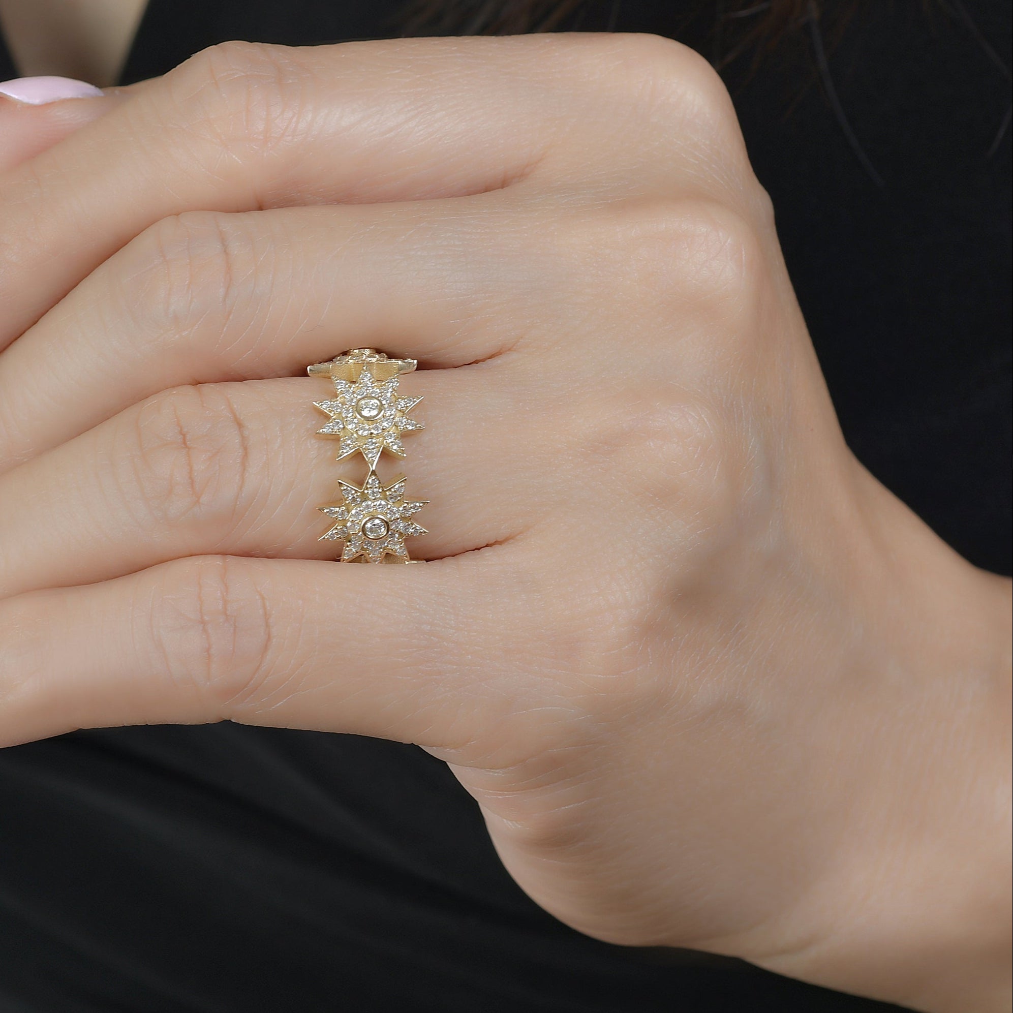 Close-up of a hand wearing a gold ring with a diamonds on a neutral background