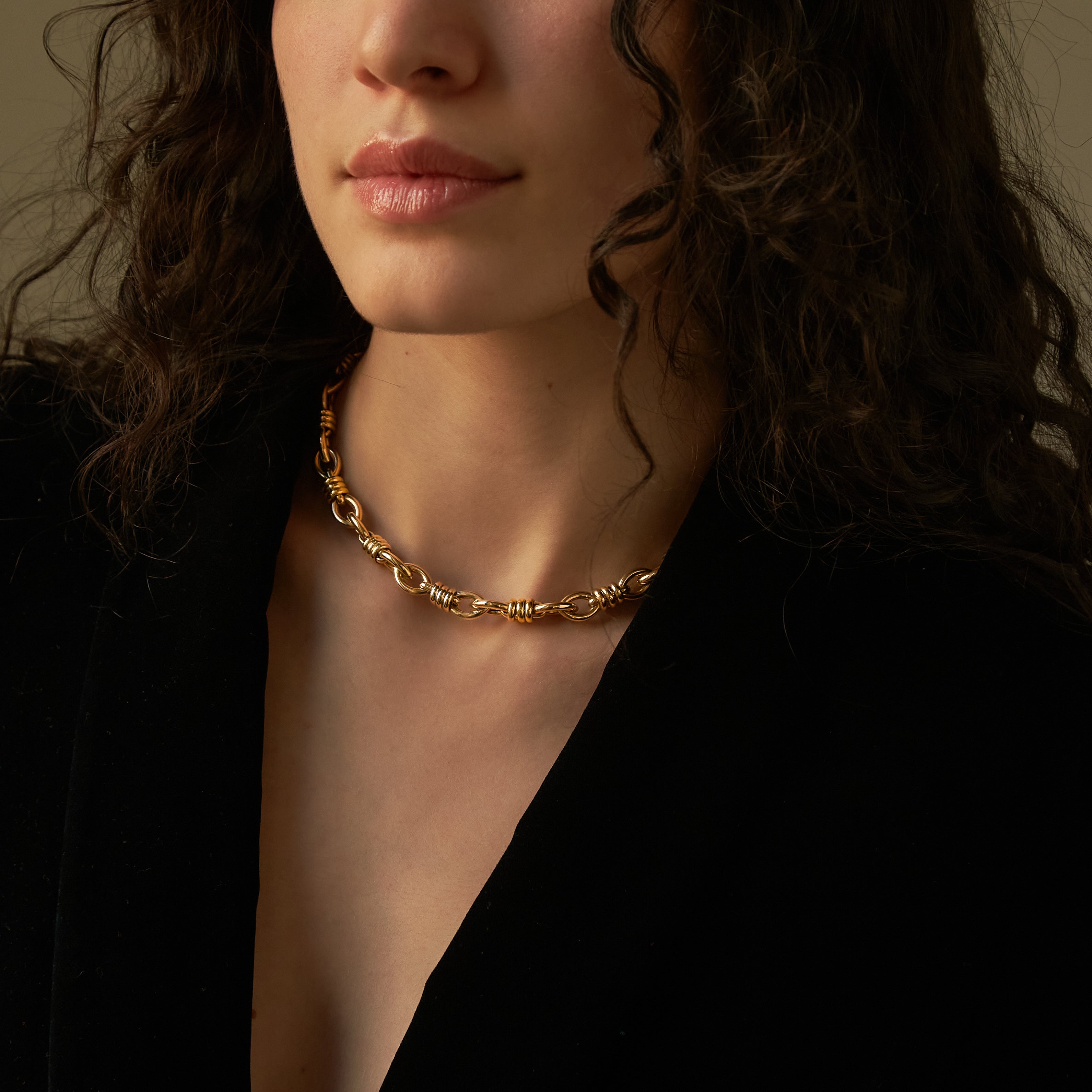 Woman wearing a gold chain necklace against a dark background