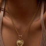 Gold necklace with a heart-shaped pendant on a person wearing a beige top.