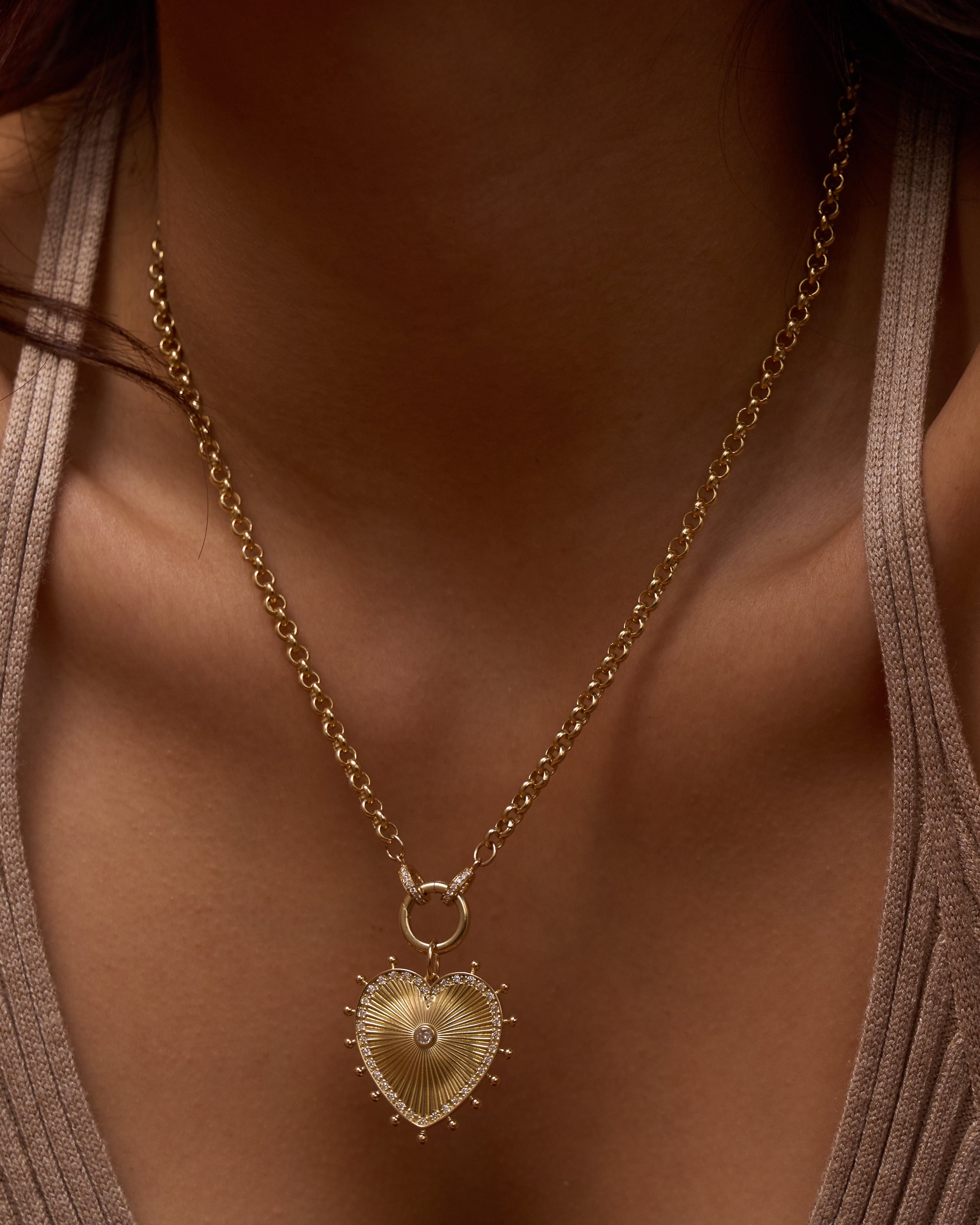 Gold necklace with a heart-shaped pendant on a person wearing a beige top.