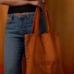 Person holding an orange tote bag with 'Lionheart' branding against an orange background