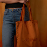 Person holding an orange tote bag with 'Lionheart' branding against an orange background