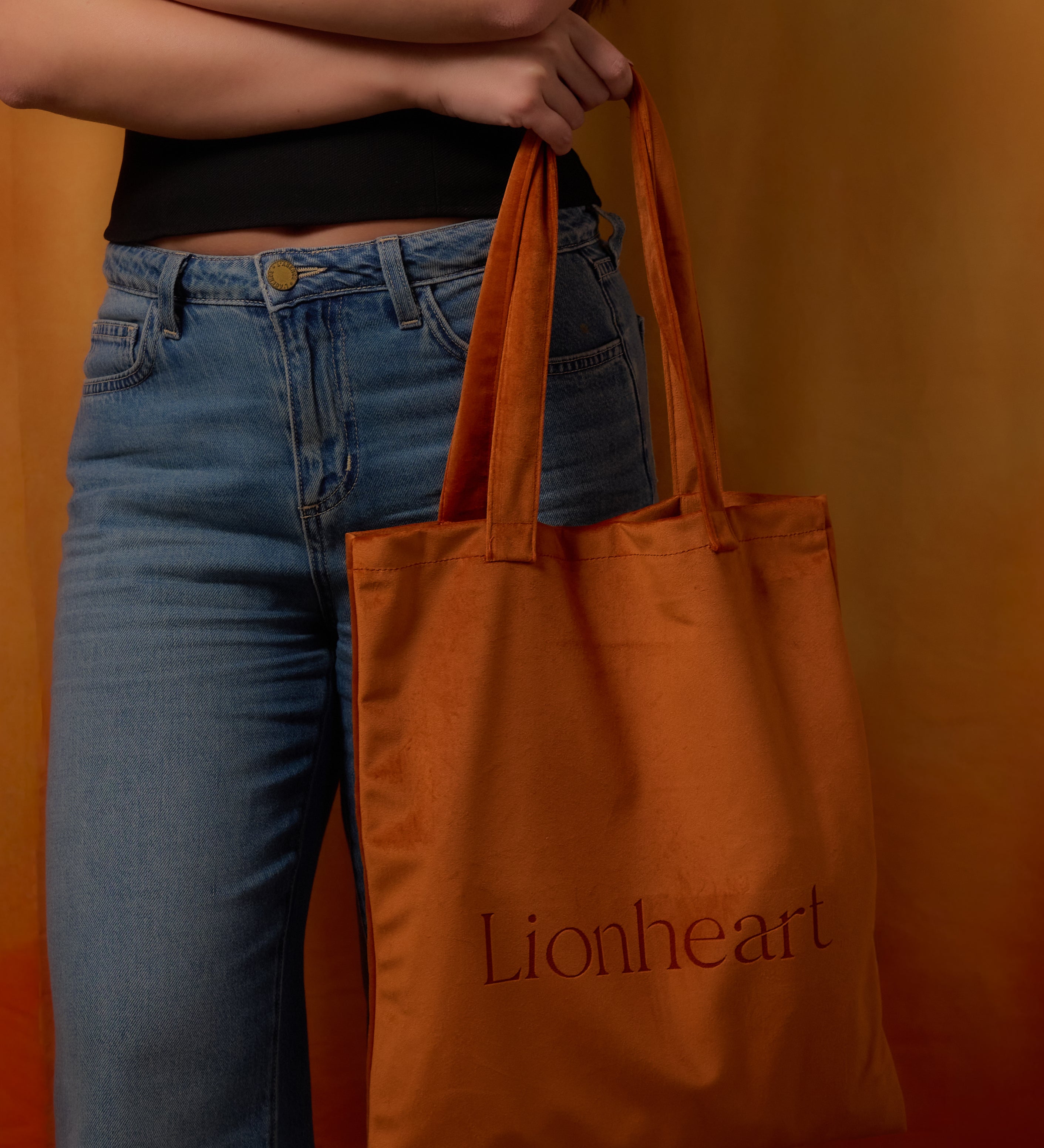 Person holding an orange tote bag with 'Lionheart' branding against an orange background