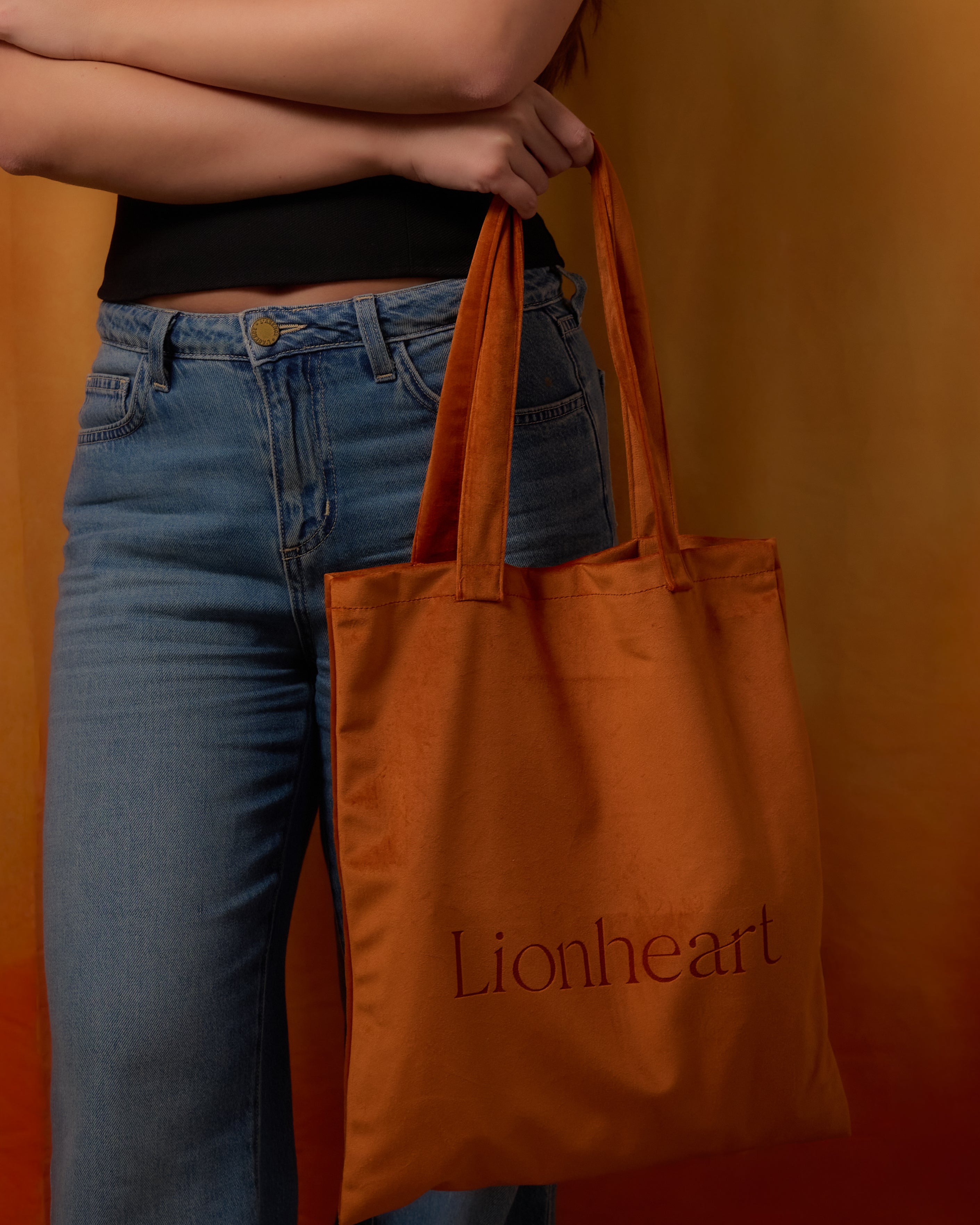Person holding an orange tote bag with 'Lionheart' branding against an orange background