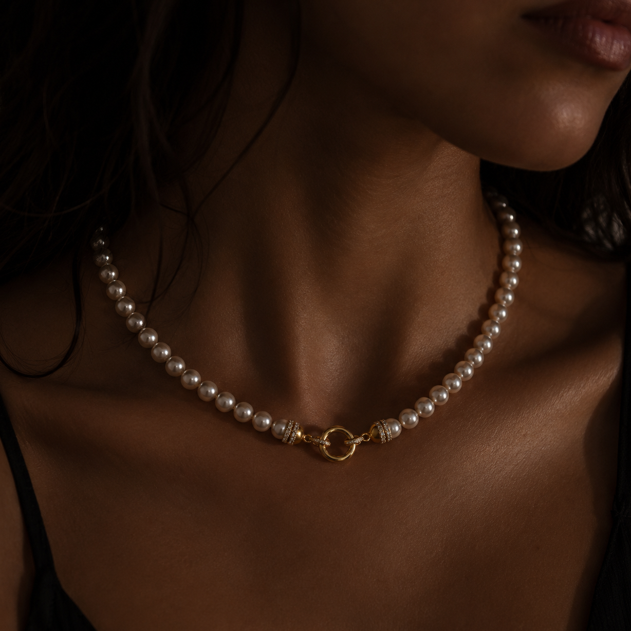 A close-up of a model wearing a delicate pearl necklace with a gold toggle clasp and diamond end caps
