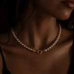 A close-up of a model wearing a delicate pearl necklace with a gold toggle clasp and diamond end caps
