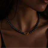 A close-up of a model's neck and chest wearing a hematite  beaded necklace with a small gold ring clasp.