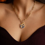 A bold lapis forest medallion with pavé diamond accents, paired with a golden horse charm and worn on a statement trombone chain