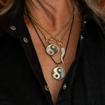 Layered in Lionheart gold chains featuring Harmony yin yang medallions with pavé diamond horn charm worn on a model in black shirt