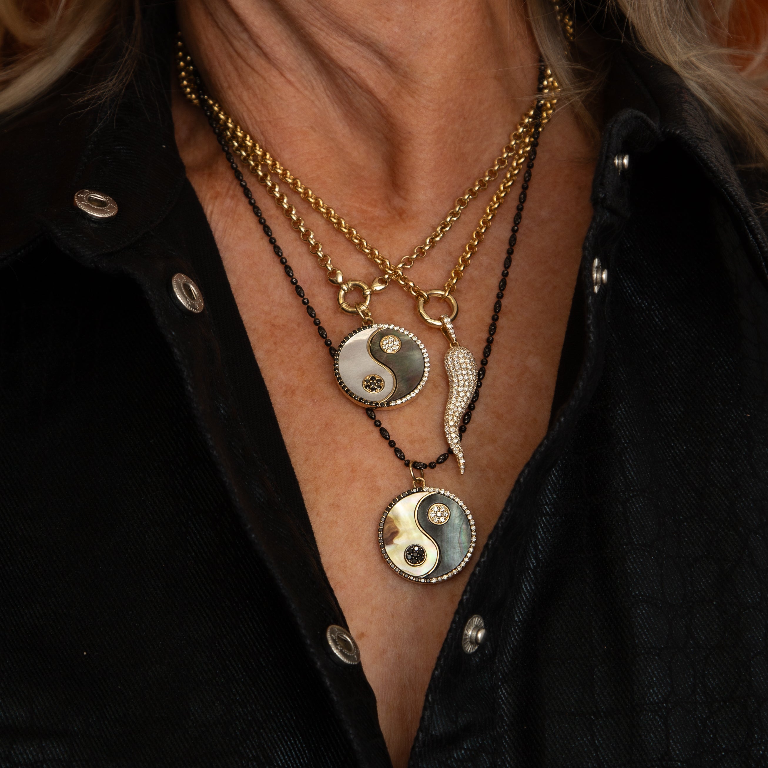 Layered in Lionheart gold chains featuring Harmony yin yang medallions with pavé diamond horn charm worn on a model in black shirt